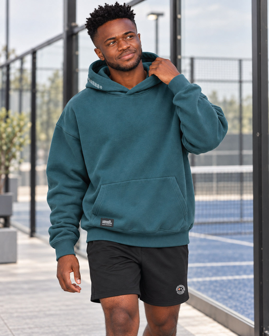Donkere-jongen-loopt-met-Oversized-Hoodie-Kairo-op-een-padelclub